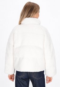Witte, fluffy, textuurjacket met een hoge kraag, oversized silhouet en horizontale stikdetails. Draag het met blauwe jeans.