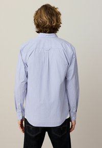 Cămașă button-up de culoare albastru deschis, cu dungi verticale albe, mâneci lungi, pliu la spate și hem rotunjit. Materialul pare neted și respirabil.