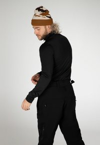 Maglietta nera a maniche lunghe e pantaloni neri, che mostrano un design aderente. Berretto a scorrimento marrone e crema con polsino a coste, maglia texturizzata.
