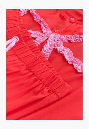 Jasně červená tkanina s elastickým pasem a světle růžovým volánkovým lemováním na knoflíkovém oděvu.