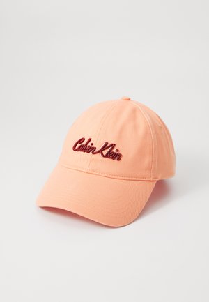 Peach cotton baseball cap with a curved brim and embroidered "Calvin Klein" logo in burgundy on the front. Smooth texture, adjustable strap at back.