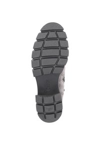 Semelle d'une chaussure avec un motif de relief en caoutchouc noir, présentant des rainures pour traction et un matériau gris clair sur le dessus.