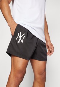 Pantalones cortos deportivos negros con un logo blanco de los New York Yankees, fabricados con un tejido ligero, que cuentan con un bolsillo lateral y un ajuste cómodo.