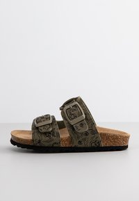 Sandalia de slide verde con estampado, dos hebillas ajustables, plantilla de corcho y suela de goma negra texturizada.