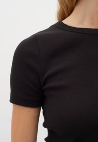 Svart ribbad kortärmad topp med rundad halsringning, har en mjuk textur och en figurnära design. Tyget har subtila linjer från ribbningen.