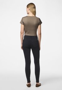 Tettsittende olivengrønn topp med korte ermer, kombinert med tettsittende svarte jeans og sko med dyreprint, sett fra baksiden.