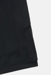 Close-up de calções atléticos pretos mostrando o logotipo Nike Swoosh costurado e painel lateral de malha respirável.