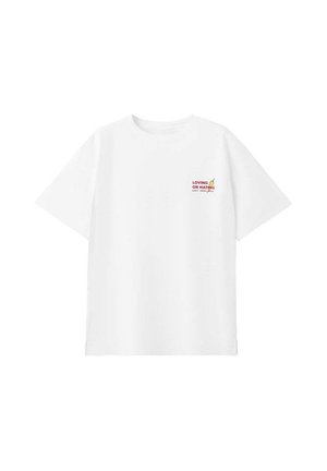 Hvid T-shirt med korte ærmer med lille rød tekst "LOVING OR HATING" og en gul chili peber grafik på den øverste venstre bryst.