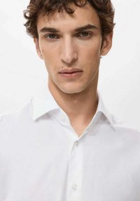 Biała koszula zapinana na guziki z klasycznym kołnierzykiem, wykonana z gładkiego materiału o subtelnym połysku, bez widocznych wzorów czy akcentów.