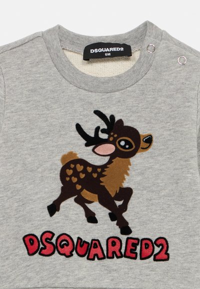Pelēks krekls ar īsām piedurknēm, kas izceļas ar brūnu ziemeļbrieža grafiku ar sirds rakstiem un sarkanu uzrakstu "DSQUARED2" zem tā. Sudraba spiedpogas plecu daļā.