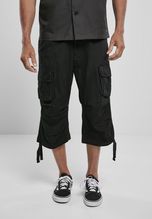 Black cargo shorts with side pockets, knee-length, made from durable fabric. Pair of black sneakers with white laces completes the look.