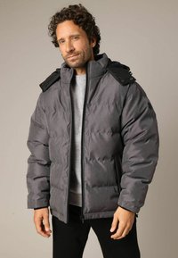 Grijze gewatteerde jas met een hoge kraag en zwarte accenten. Voorzien van een volledige rits, lange mouwen en een gladde textuur.