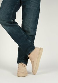 Scarpe in suede beige con una suola in gomma spessa e chiara, abbinate a jeans in denim blu scuro, leggermente arrotolati alla caviglia.