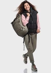 Grauer Rucksack mit glänzender Oberfläche, schwarze Steppweste, pinker Sweatshirt und olivgrüne Hose. Die Sneakers sind mit braunen und grauen Akzenten versehen.