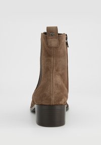 Hnědá semišová kotníková bota s nízkým podpatkem, vybavená bočním zipem a pevným zadním poutkem pro snadné nazouvání.