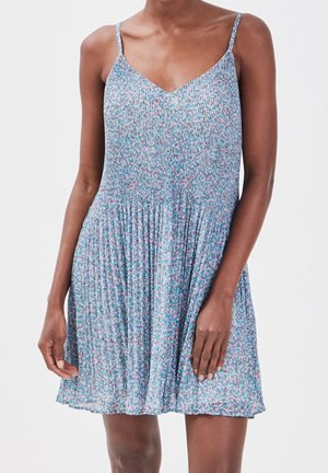 Femme portant une robe d'été bleue fleurie sans manches avec une jupe plissée et des fines bretelles.
