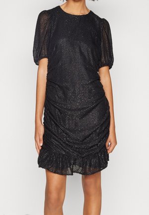 Robe noire texturée longueur genoux avec manches courtes bouffantes et ourlet volanté portée par une personne les mains détendues le long du corps.
