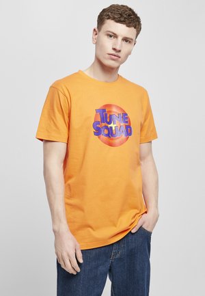 Orange bomulds T-shirt med et cirkulært grafik med "TUNE SQUAD" i fed blåt tekst, sat mod en gradient baggrund.