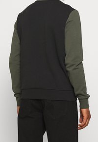 Sudadera negra y oliva con cuello redondo, mangas en contraste, puños y dobladillo acanalados. La tela parece suave con una textura lisa.