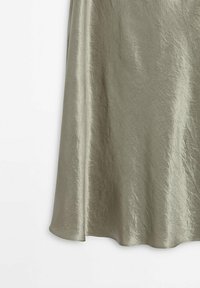 Jupe en tissu satin gris clair avec un éclat subtil et des plis doux suspendue sur un fond blanc uni.