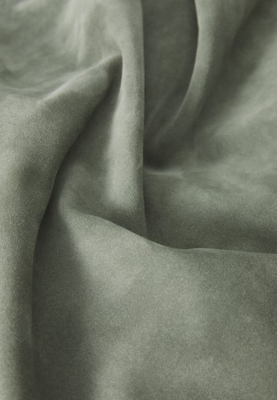 Pehmeä, teksturoitu kangas hillityssä vihreässä sävyssä, jossa on lempeät laskokset ja sileä pinta, jossa on hienovarainen kiilto, joka on tyypillistä mokalle.