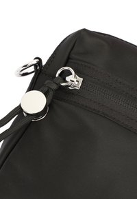 Black nylon bag corner featuring a silver zipper, toggle closure with circular hardware, and textured fabric.