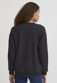 Maglione felpa nero con scollatura a girocollo, spalle scese, polsini e orlo a coste, realizzato in un morbido tessuto testurizzato.
