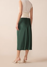 Jupe midi en satin vert avec une texture lisse, dotée d'une taille cintrée et d'une forme évasée, associée à des escarpins beige à bride au talon.
