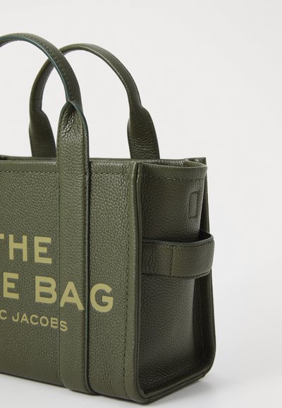 Groene leren tote bag met een gestructureerde afwerking, dubbele handgrepen en een zijvak. Heeft opvallende tekst aan de voorkant in een lichte kleur.