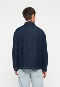 Dark blue denim jacket with a collared neckline, long sleeves, and a relaxed fit. Additional light stitching and a straight hem.