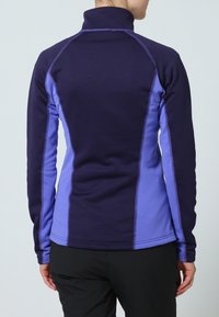 Fioletowa i lawendowa bluzka z długim rękawem, charakteryzująca się wysokim kołnierzem, teksturowanym materiałem oraz kontrastowymi panelami bocznymi z detalami szycia.