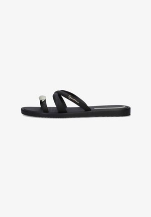 Sandalo nero piatto con anello per l'alluce e due sottili cinturini che attraversano il piede, con marchio "Ipanema" in oro su un cinturino.