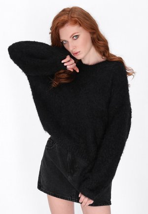 Zwarte fuzzy trui van textuur materiaal met een brede halslijn en verlaagde schouders, gecombineerd met een hoge taille zwarte denim rok.