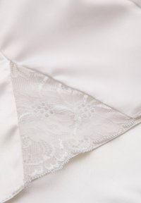 Siden i mjukt vitt med en spetspanel som har blommönster. Spetsens kant är vågig, vilket kontrasterar med den släta texturen av silken.