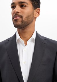 Dark gray blazer with a textured finish, notch lapel, and a single pocket. Paired with a crisp white dress shirt featuring buttons.