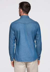 Chemise en jean pour homme de couleur bleu moyen, avec col boutonné, manches longues avec poignets à boutons, et ourlet arrondi. Texture unie.