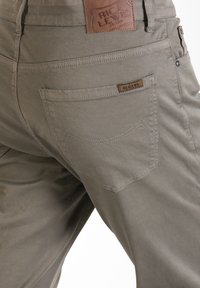 Pantalons croppés kaki avec un patch en cuir marron, couture visible des poches arrière et texture de tissu en coton lisse.