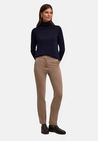 Marineblauer Rollkragenpullover kombiniert mit beigefarbenen, schmal geschnittenen Hosen. Die Hosen haben Taschen; der Pullover ist gerippt und sorgt für eine weiche Textur. Schwarze Schuhe vervollständigen den Look.