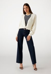 White ribbed cardigan over a navy and white striped top, paired with dark blue wide-leg jeans and black heeled sandals.