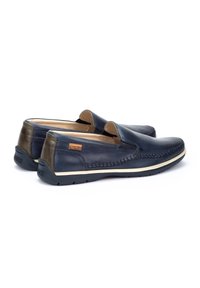 Zapatos de cuero de color navy de tipo slip-on con acentos marrones en contraste, detalle de costura y suela de goma. Presentan una etiqueta de la marca en el lateral.