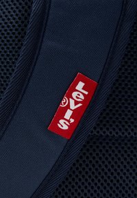 Section de tissu en maille bleu marine présentant une étiquette rouge Levi's avec du texte blanc. Le matériau principal est robuste, avec une texture lisse et un design respirant.
