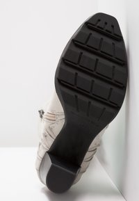 But z fakturą w jasnobeżowym kolorze, ozdobiony precyzyjnym przeszyciem, z wytrzymałą czarną gumową podeszwą wyposażoną w wzorzysty bieżnik i podniesiony obcas.