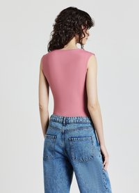 Body rosa senza maniche con una texture liscia, abbinato a jeans di denim azzurro chiaro a vita alta con cuciture visibili e tasche.