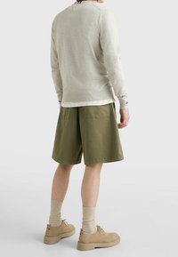Suéter gris claro de manga larga sobre pantalones cortos verde oliva. Zapatos de ante color arena con calcetines gris claro. Diseño simple y casual.
