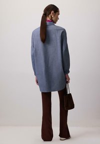 Lyseblå, oversized skjorte med lange ærmer og en tekstureret stof; parret med brune flared bukser og en mørkebrun taske.