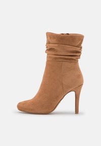 Tan suede nilon yang memiliki desain longgar, ujung runcing, dan tumit stiletto tinggi. Dilengkapi dengan penutup ritsleting di sisi dalam.