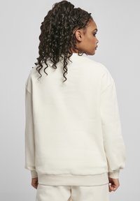 Kremfarget oversized hettegenser med rund hals og ribbestrikkede mansjetter. Myk tekstur, minimale sømmer og subtile designdetaljer.