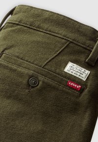 Dark green wool Levi's pants showing back pocket with button, belt loop, and Levi's branded white and red fabric tags.