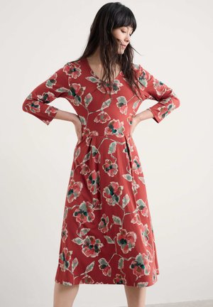 Rotes Blumenkleid mit dreiviertel Ärmeln, V-Ausschnitt und ausgestelltem Rock. Besitzt große rosa und grüne Blumen auf einem strukturierten Stoffhintergrund.