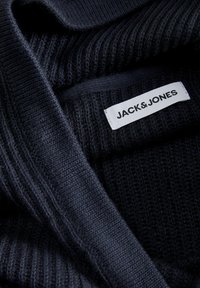 Cárdigan de punto en azul marino oscuro con textura de canalé, cuello ancho y una etiqueta visible que dice "JACK & JONES" en blanco.